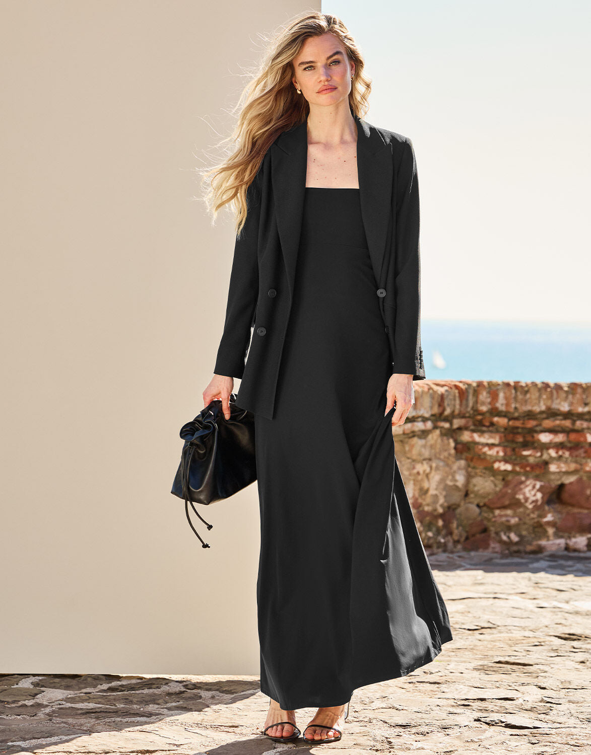 Model walking in the Saint Black dress in jersey lycra under a long black blazer.