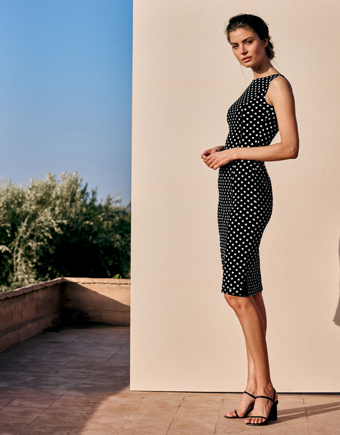 Model standing in the Gloria Ivory Small Dot dress in jersey lycra with a polka dot print.