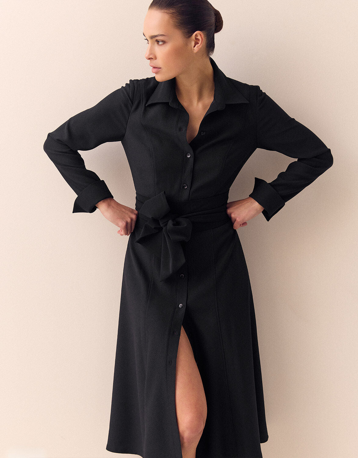 Model standing in the Catherine Black dress in crepe satin with a shirt collar and a tie belt.