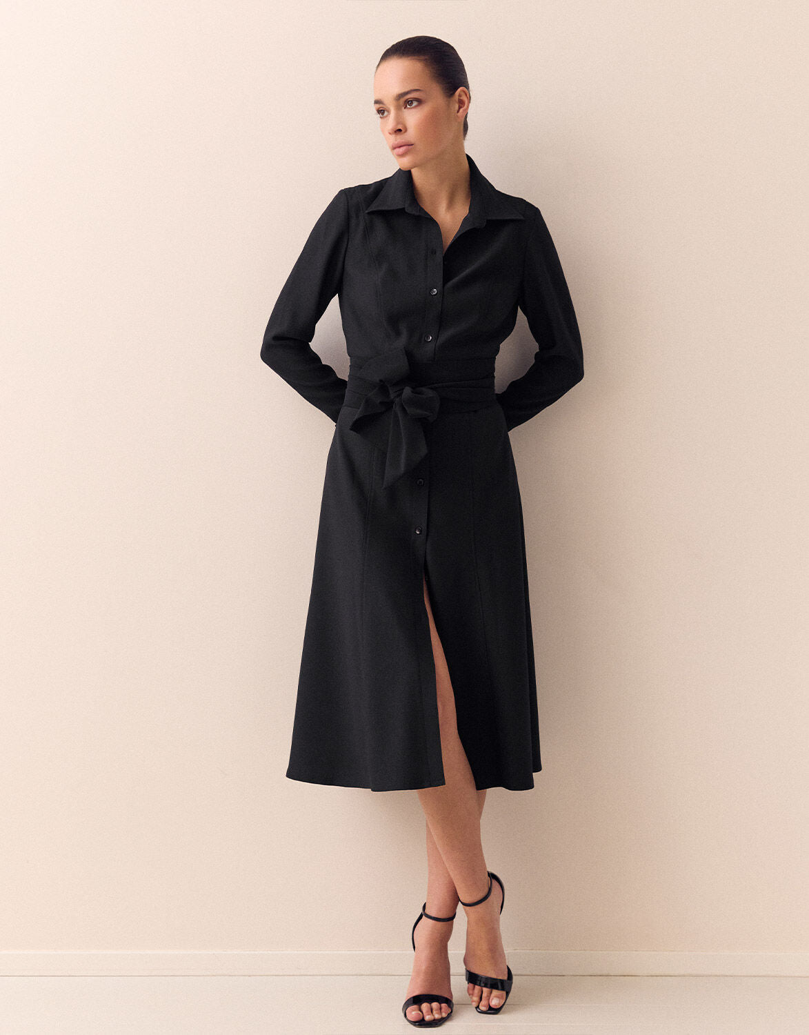 Woman in a chic, black midi dress with long sleeves and a bow tie in a minimalist, light space.