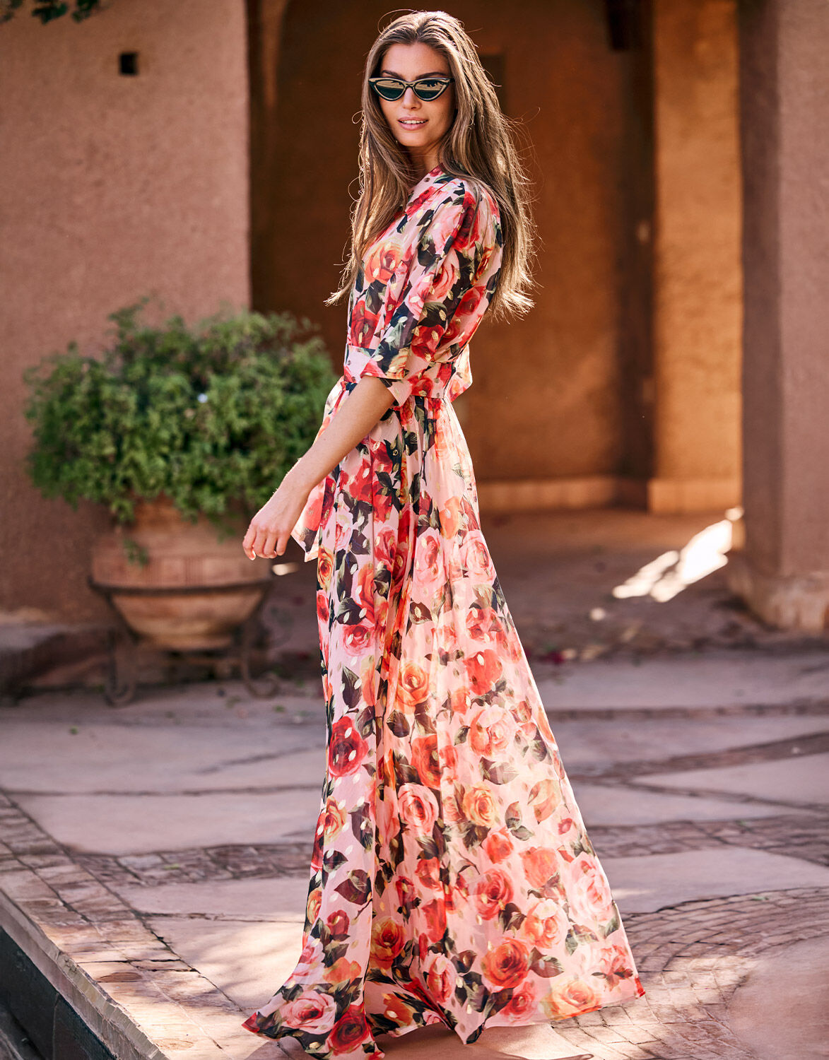 Woman in a colorful long floral dress with three-quarter sleeves poses outside on a sunny day.