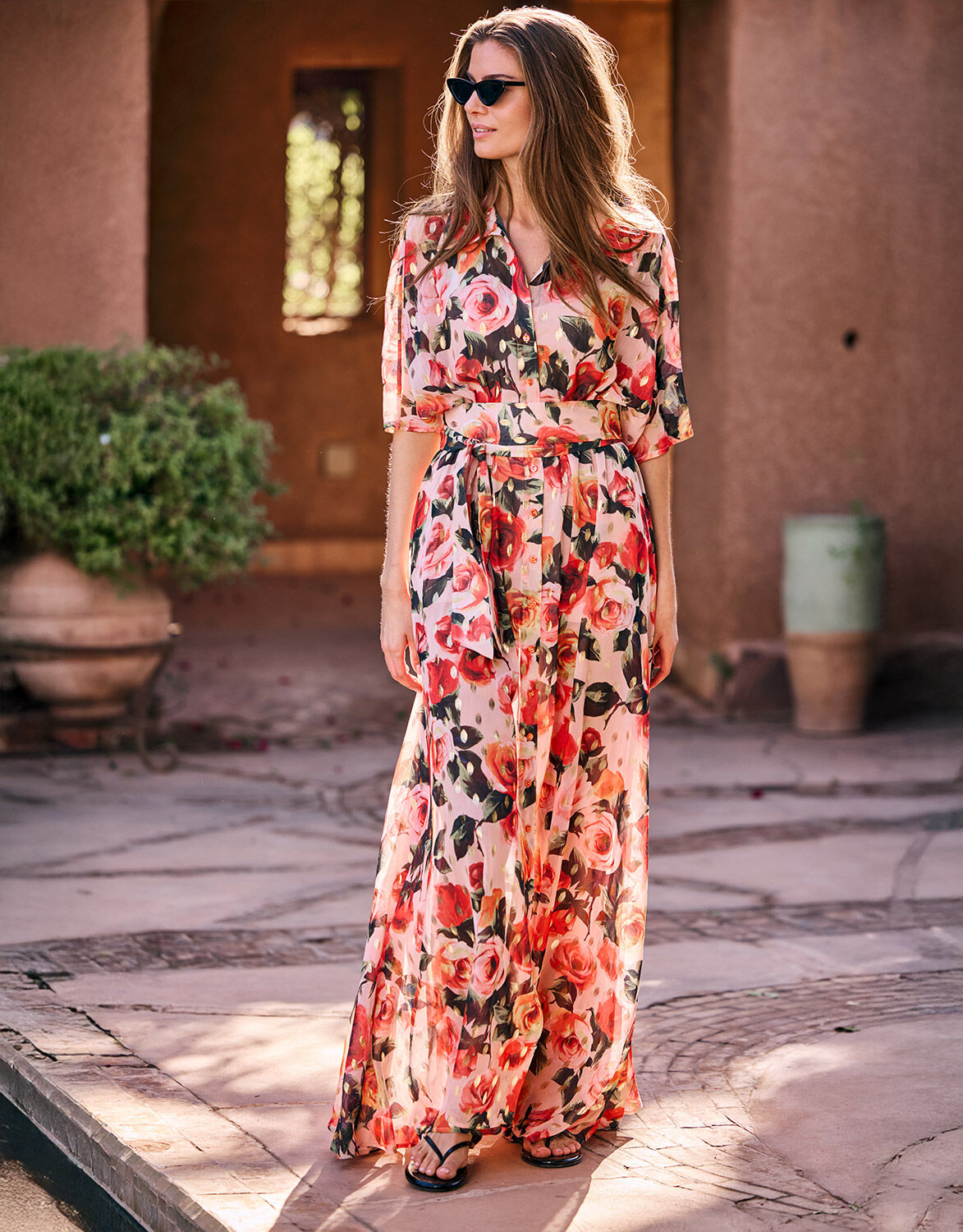 Woman in a colorful pink and red floral dress on a summer day, wearing sunglasses, elegant and stylish design.