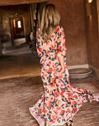 Woman in floral dress walks through cozy, earth-toned interior with wooden and brick elements.