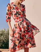 Woman in an elegant summer dress with a colorful floral print and three-quarter sleeves, outdoors in a sunny environment.