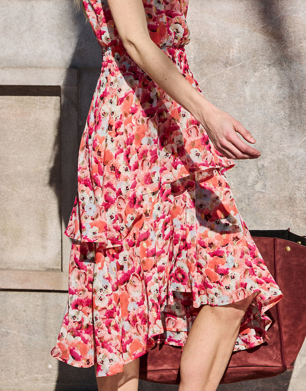 Sleeveless dress with a floral pattern in pink and red on a light-colored background, with pleats and an asymmetrical hem.