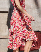 Sleeveless dress with a floral pattern in pink and red on a light-colored background, with pleats and an asymmetrical hem.