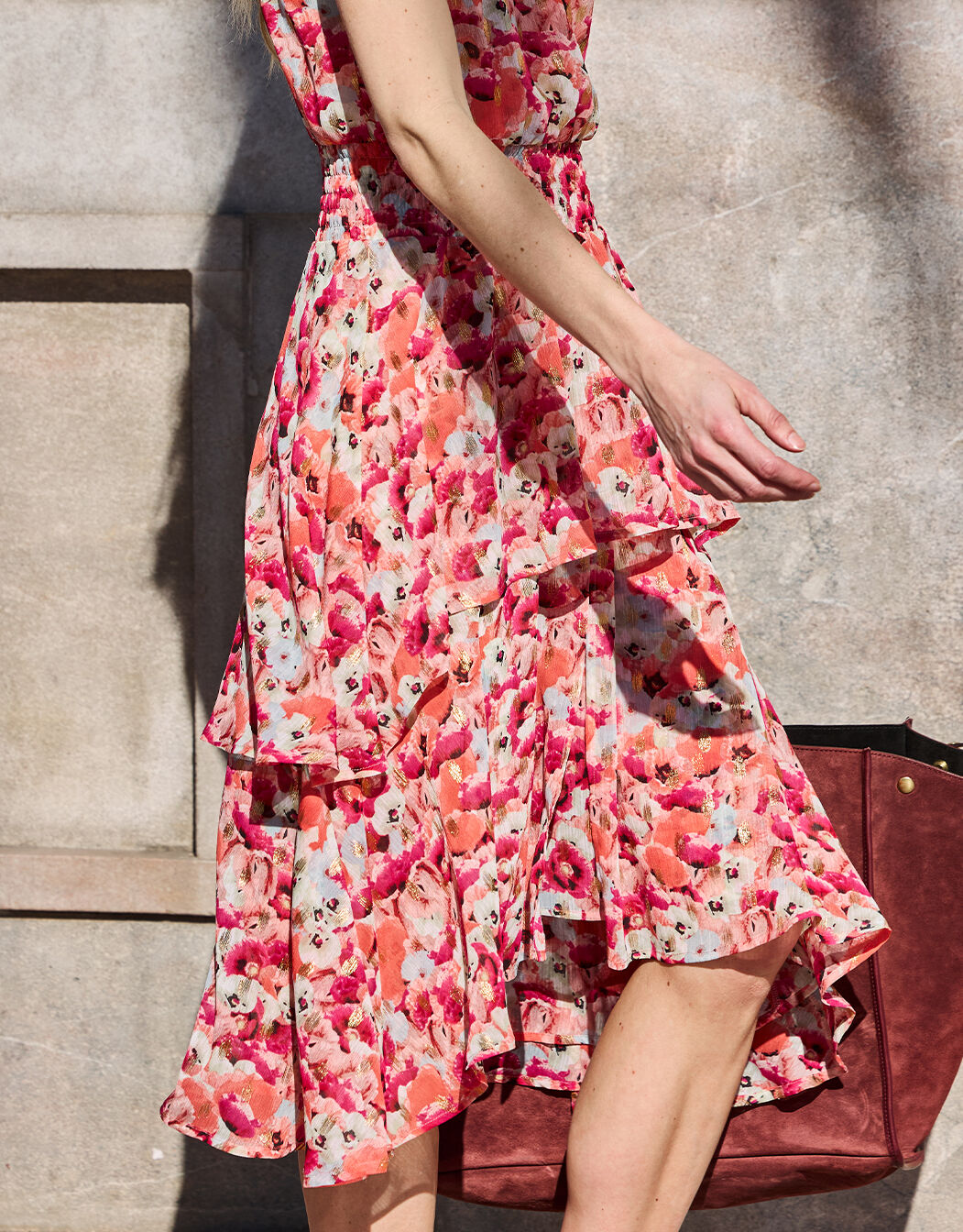 Sleeveless dress with a floral pattern in pink and red on a light-colored background, with pleats and an asymmetrical hem.
