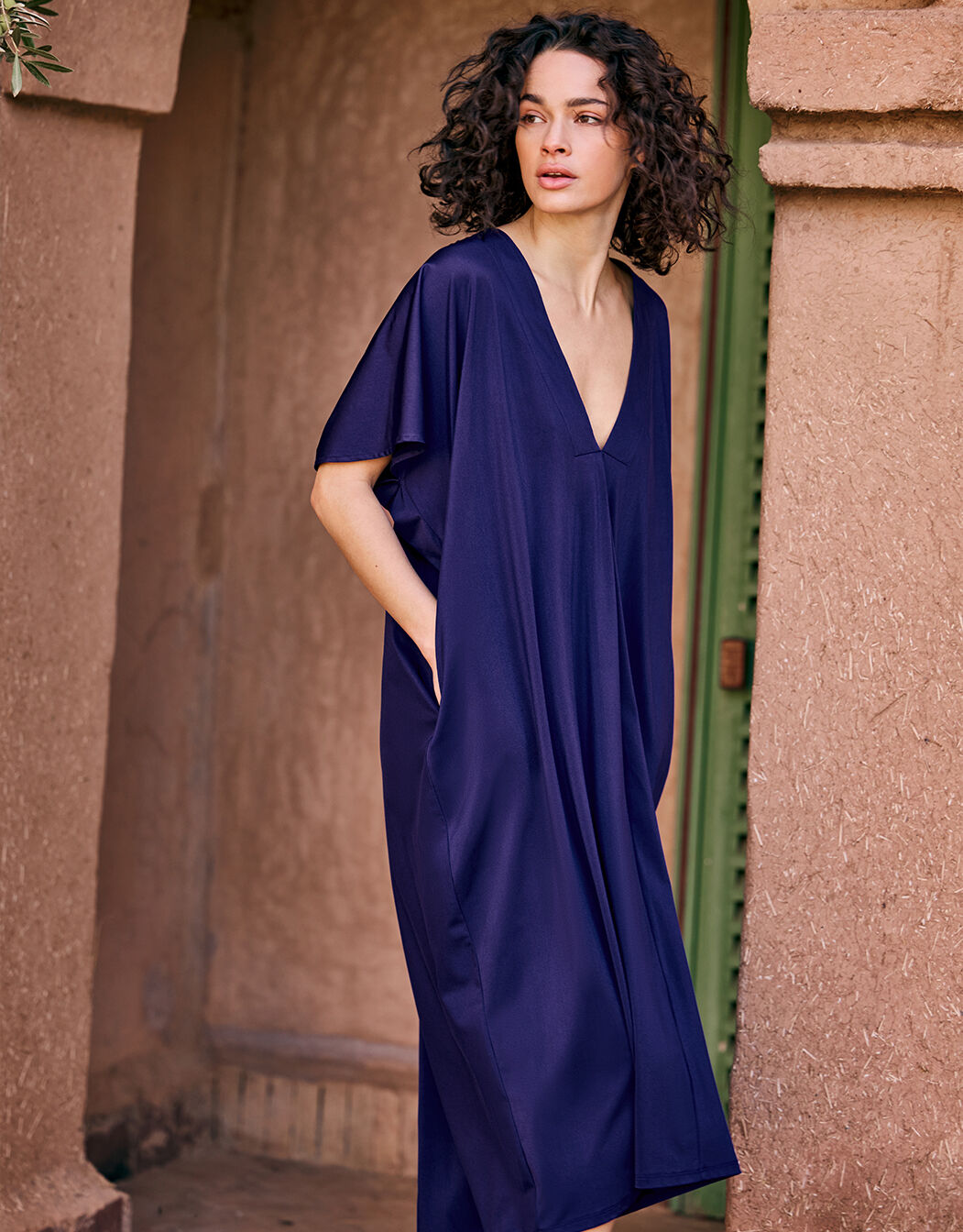 Model standing in the Francisca Shimmery blue dress in jersey lycra with a deep V-neck.