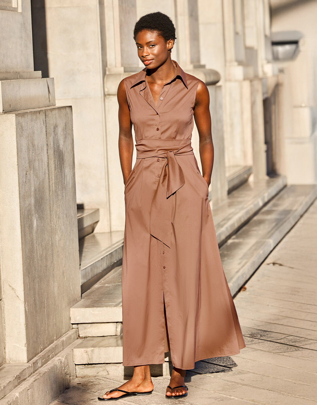 Model standing in the Emilia Cacao dress in cotton stretch poplin with a tie belt.
