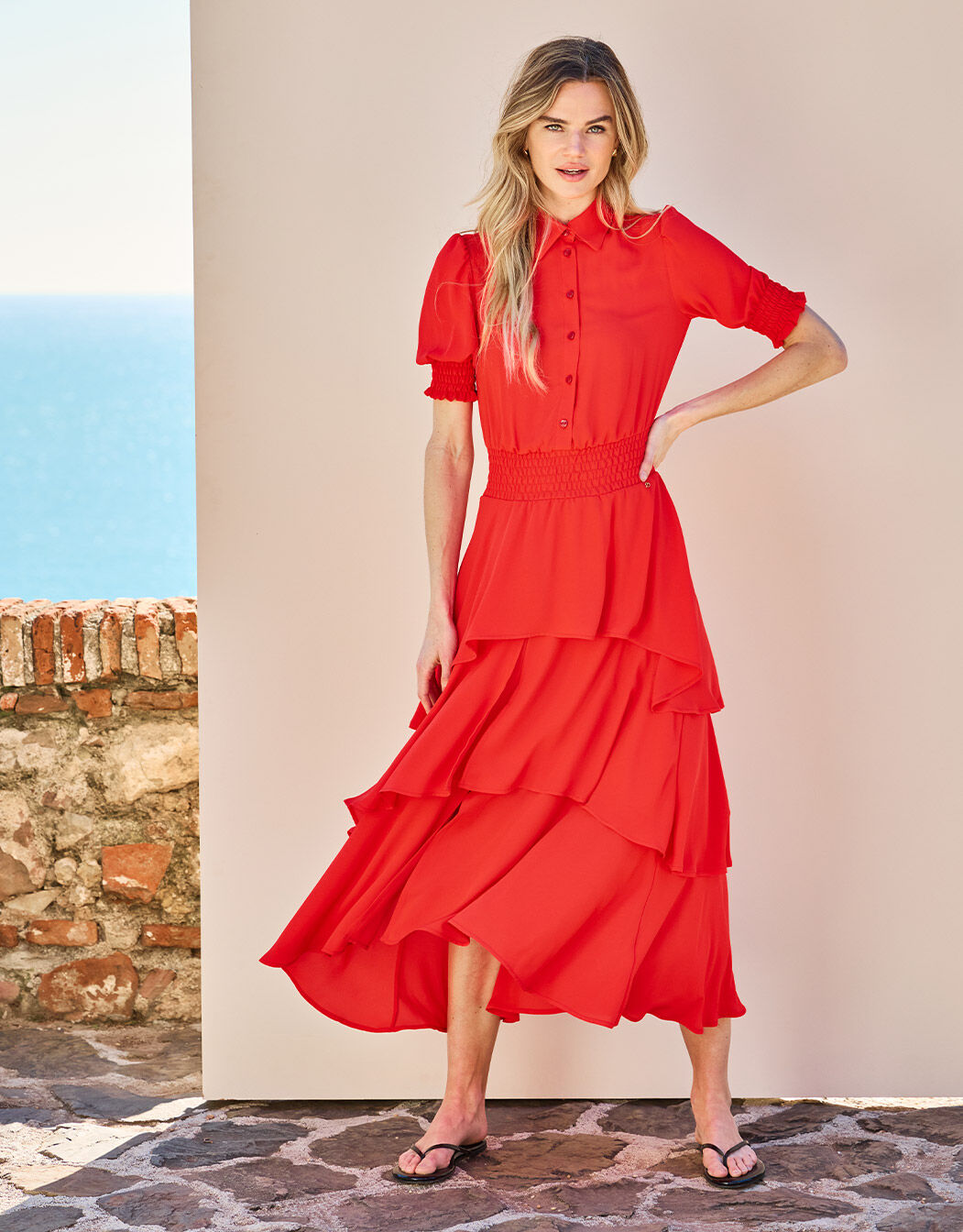 Model standing in the Kiki Hibiscus dress in crepe georgette with a tiered ruffled skirt.