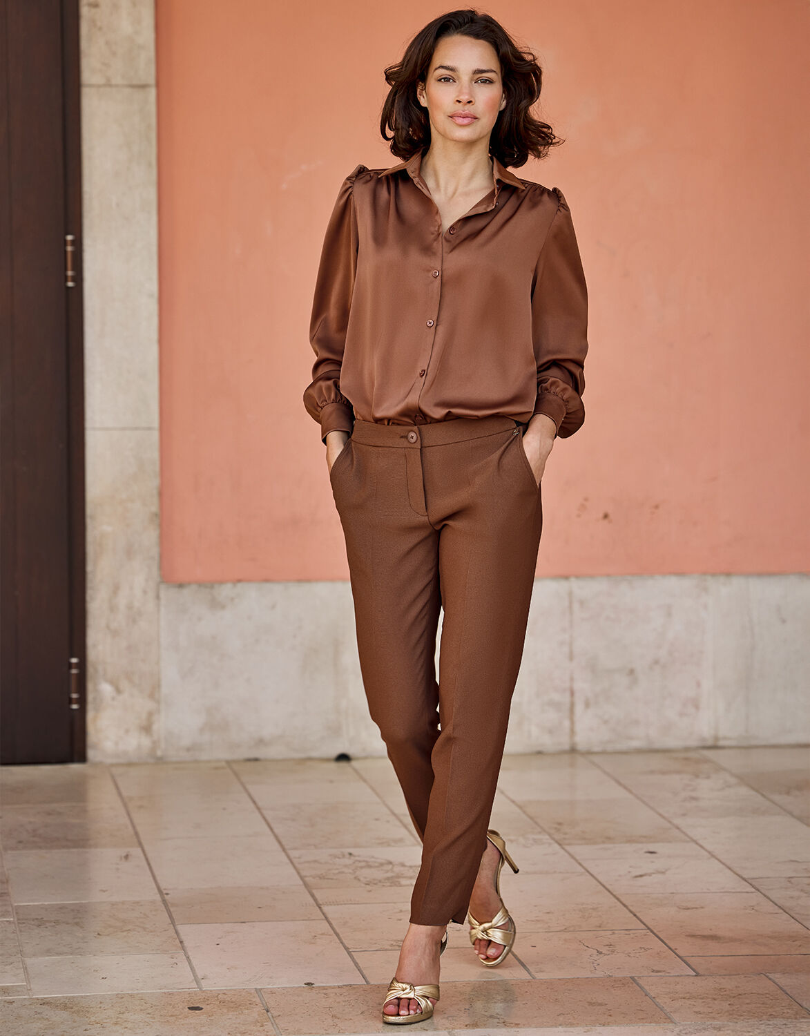 Model standing in the Seoul Cacao Brown trousers in crepe satin with a matching blouse.