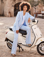 Woman in a pastel blue suit sitting on a vintage white scooter, relaxed posture with a stylish appearance.