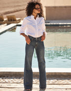 White long-sleeved blouse and straight, dark blue jeans, worn by a model in front of a modern swimming pool.
