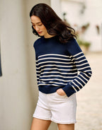 Woman poses in casual outfit with dark blue striped sweater and white shorts, summer fashion collection.