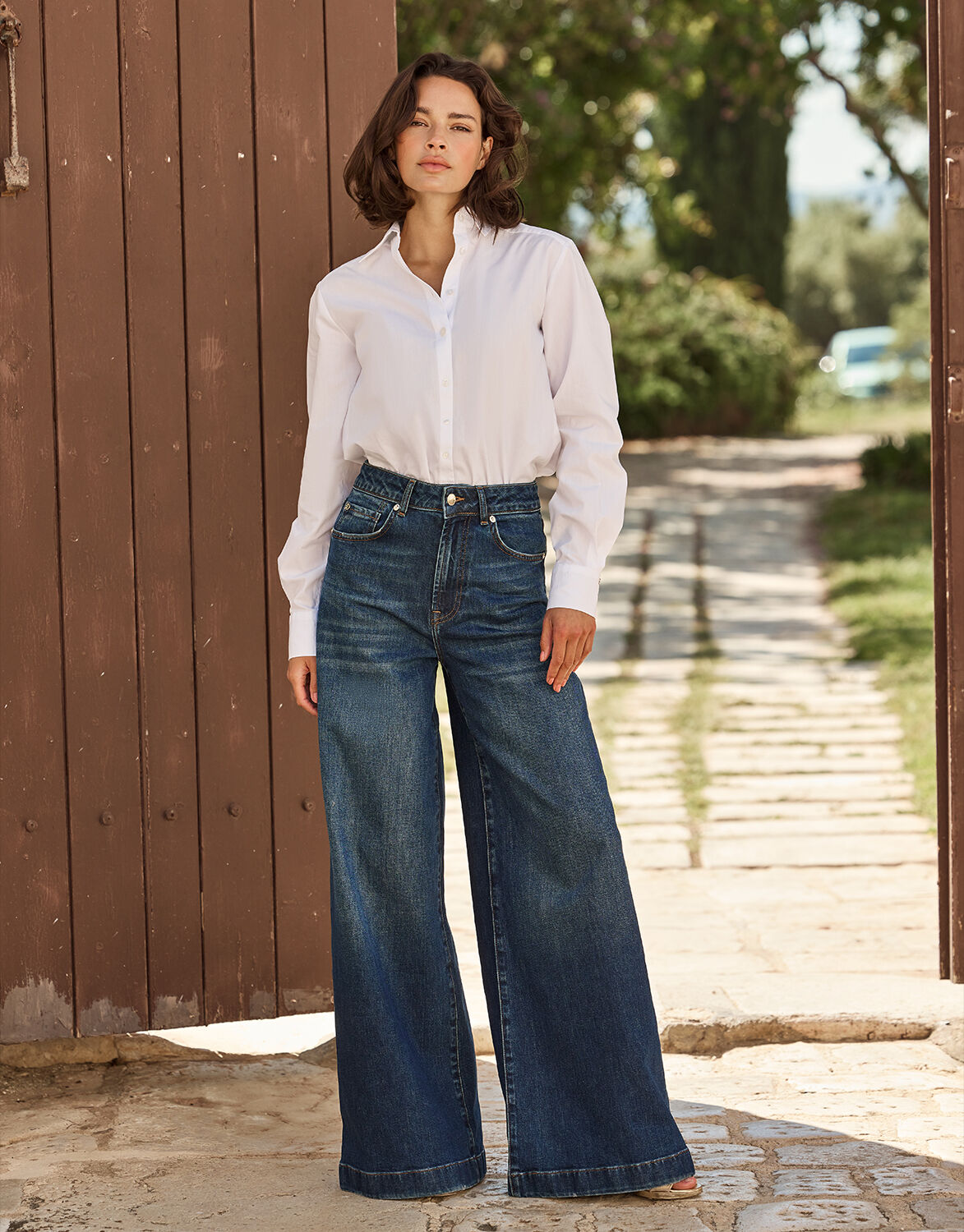Model standing in the Melina Washed Indigo jeans in stretch cotton with a white blouse.