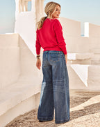 Woman in a red sweater with loose jeans on a white architectural stone staircase under a blue sky in the sun.