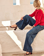 Woman in a casual red sweater and baggy jeans sitting on white stone steps, summery atmosphere.