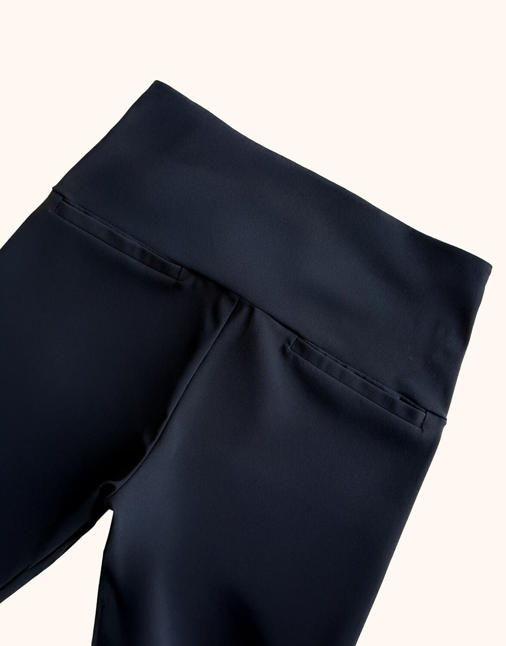 Black women's trousers with a wide waistband and decorative pockets, made of smooth fabric, close-up of the top.