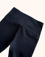 Black women's trousers with a wide waistband and decorative pockets, made of smooth fabric, close-up of the top.