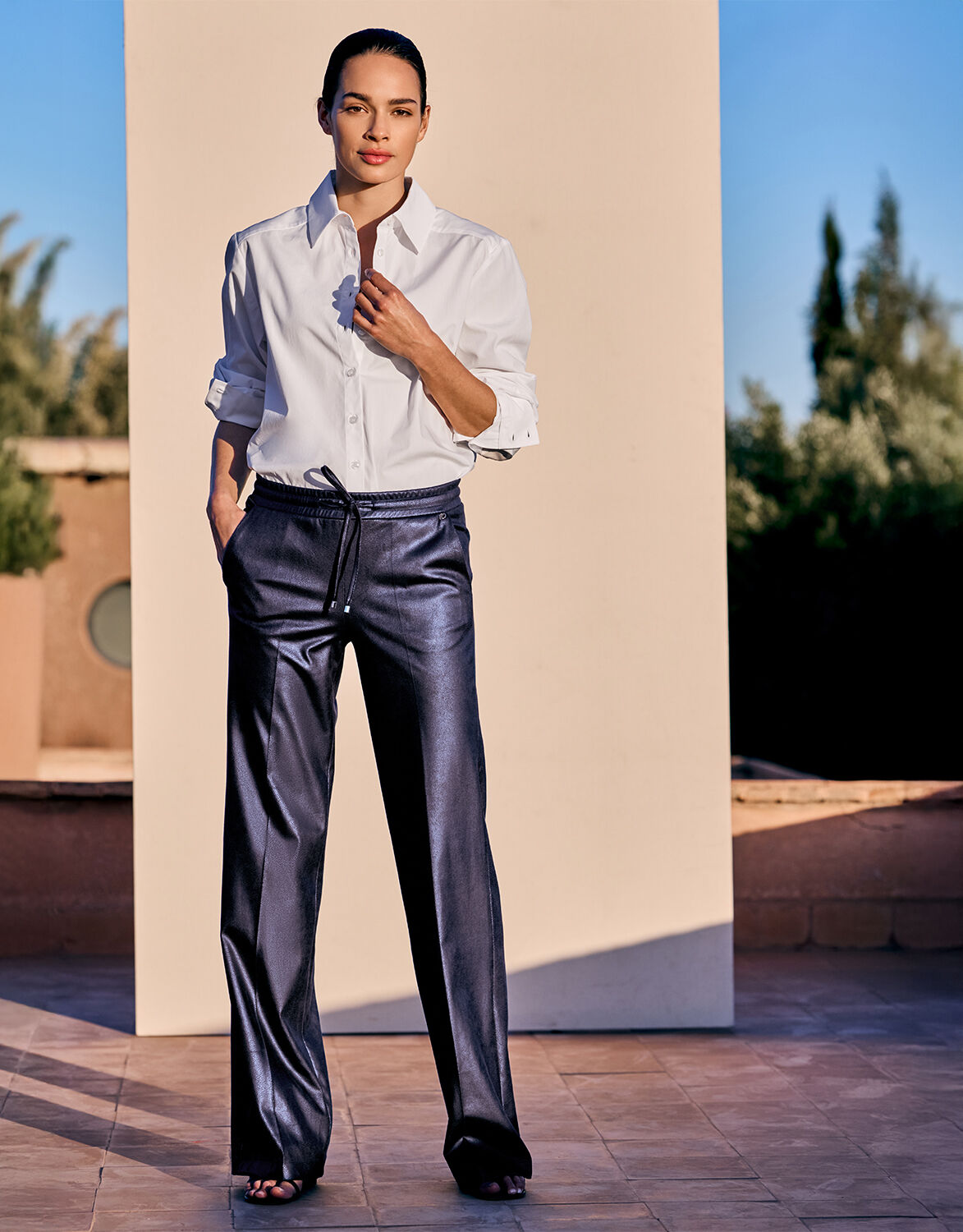 Model standing in the Nova Midnight Plum trousers in leather look with a white shirt.