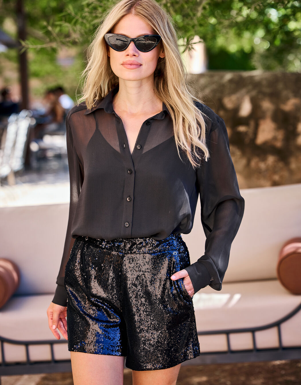 Model standing in the Roxy Black shorts in sequins with a sheer black blouse.