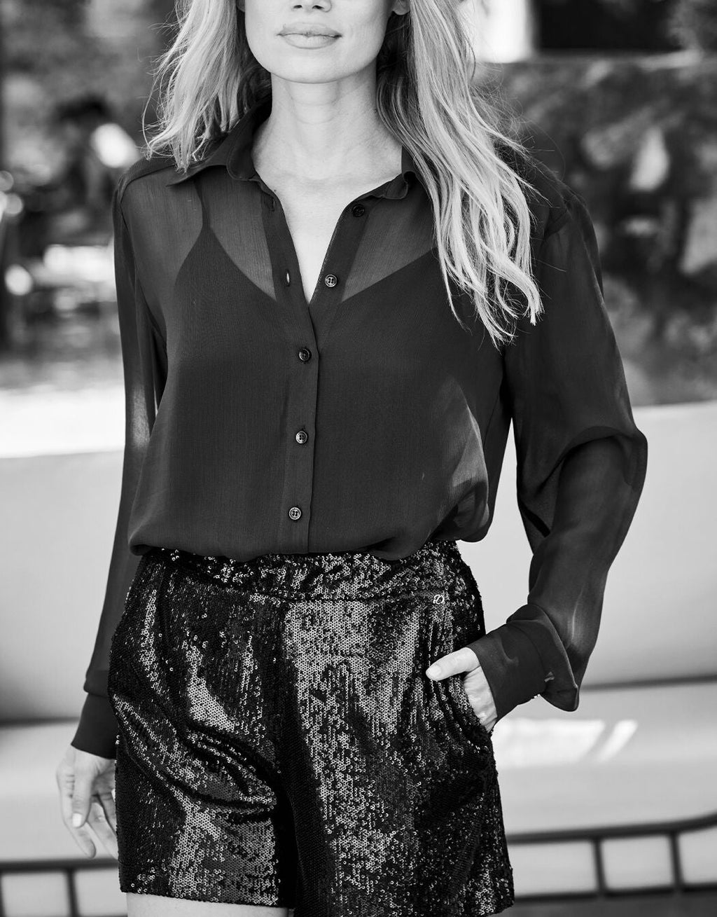 Black and white photo of a woman in a see-through blouse and glittering shorts, casual elegant fashion.