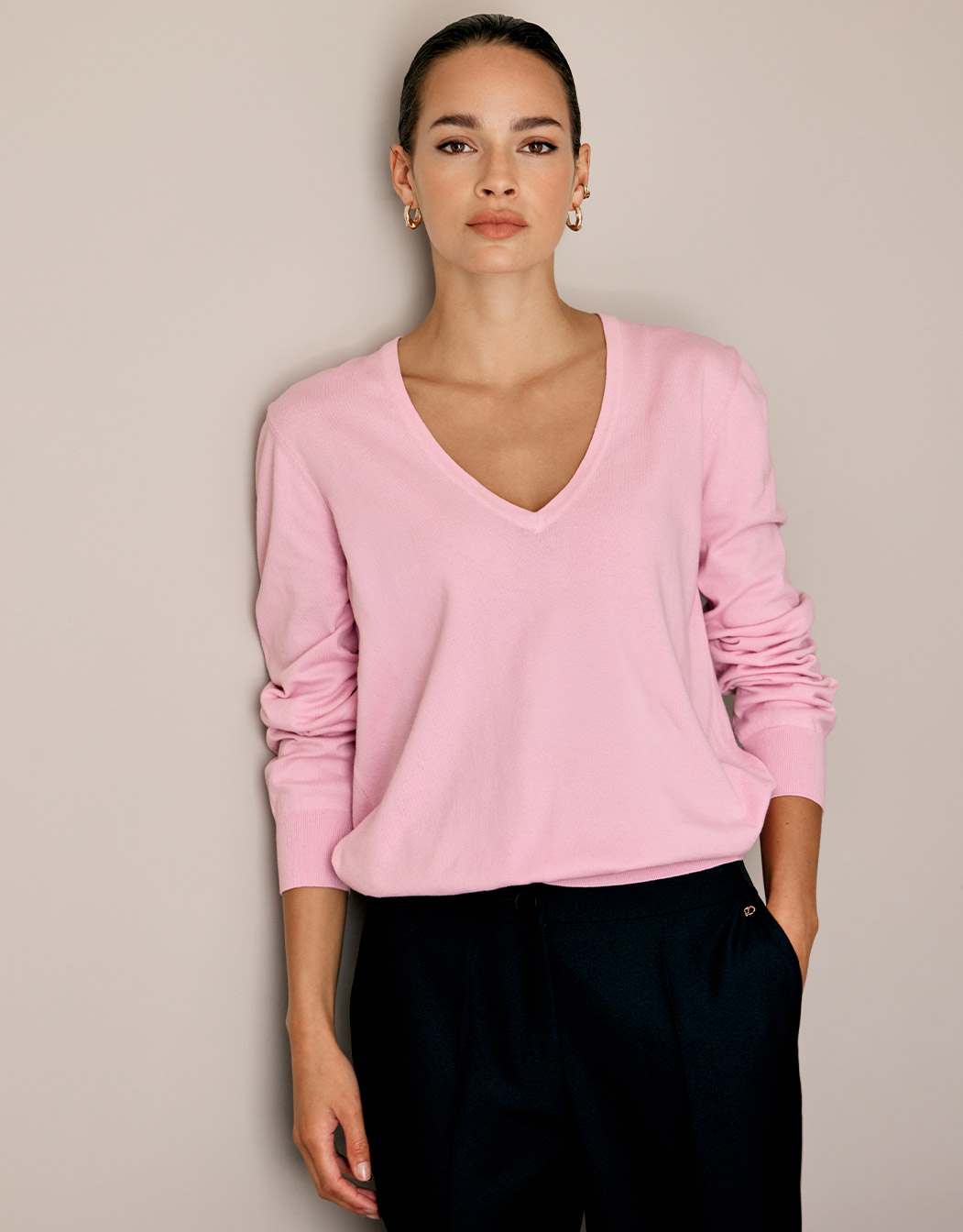 Model standing in the Loretta Pale Rose jumper in organic cotton knit with a V-neck.