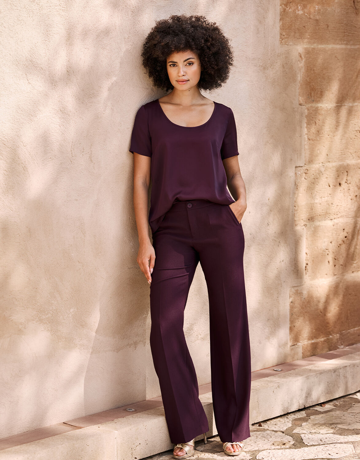 Model standing in the Geneva Deep Aubergine trousers in crepe satin with a matching top.