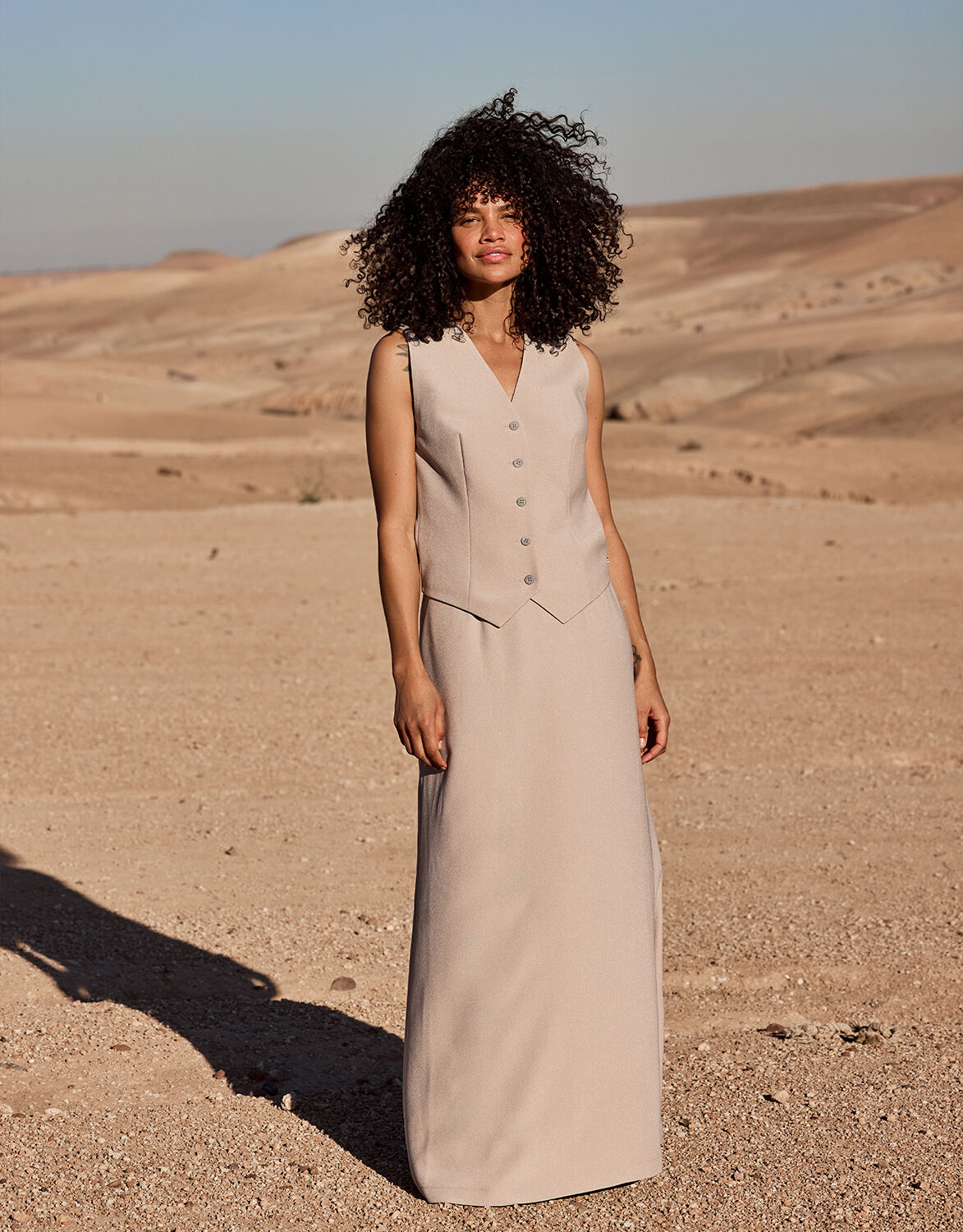 Model standing in the Christy Pebble skirt in crepe satin with a matching waistcoat in a desert.