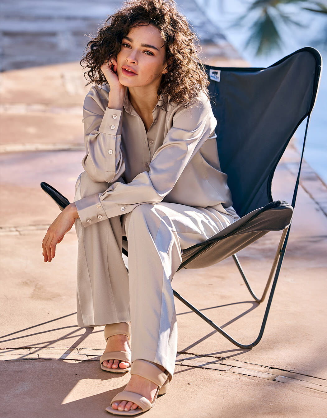 Model seated in the Estee Pebble blouse in satin with matching wide trousers.