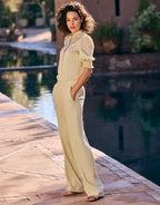 Elegant woman in a fashionable beige blouse with gathered sleeves and matching trousers, standing by a swimming pool.