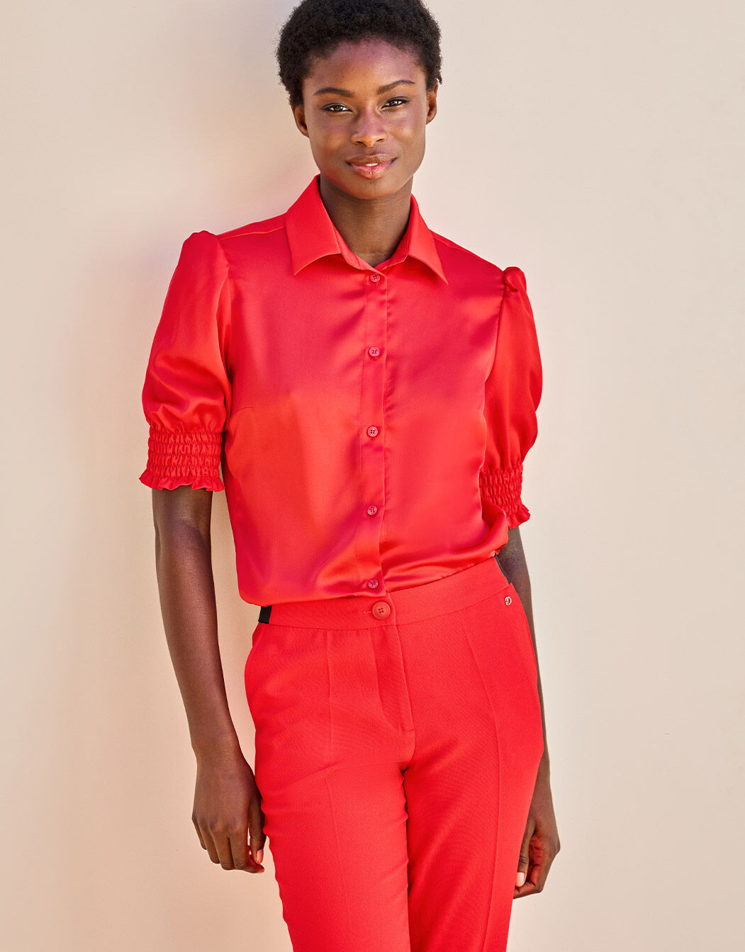 Model draagt een felrode satijnen blouse met korte pofmouwen en hoogsluitende kraag, tegen een neutrale achtergrond.