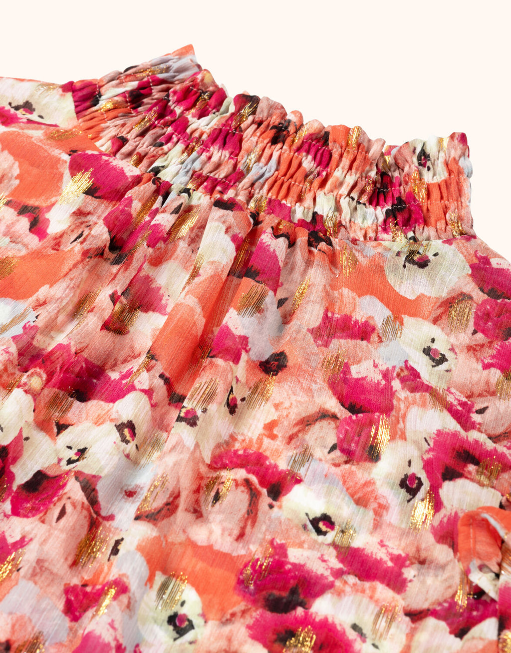 Shoulder detail of blouse with colorful floral print and gold accents, gathered neckline and soft fabric.