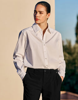 Model steht in der Cameron White Bluse aus Popeline, in eine schwarze Anzughose gesteckt.
