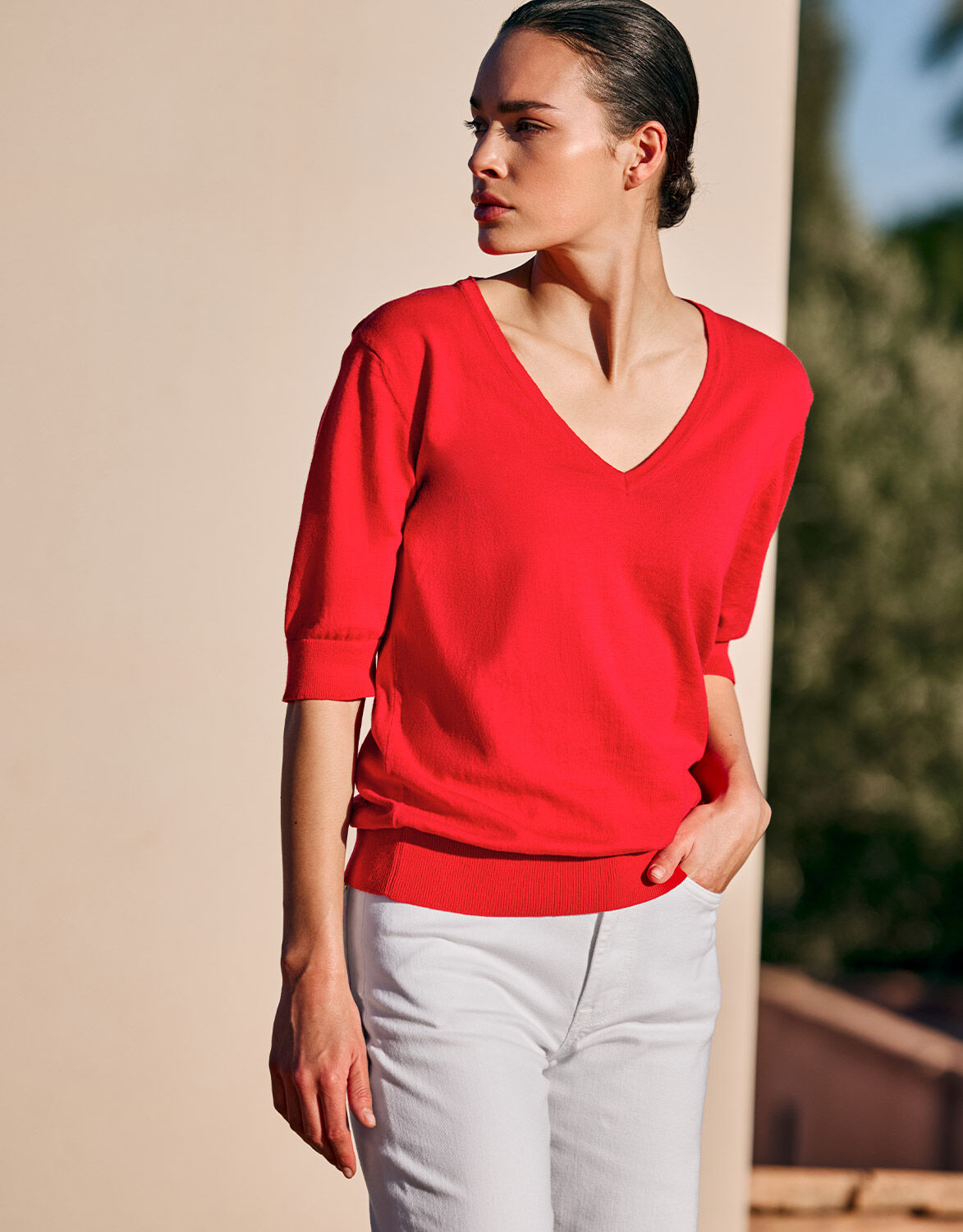 Model standing in the Marie Hibiscus jumper in organic cotton knit with a V-neck.