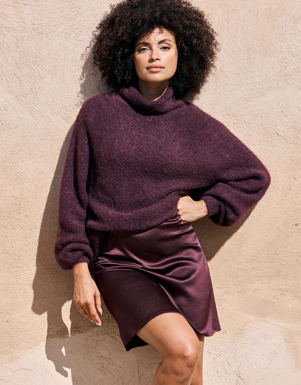 Model standing in the Giovanna Deep Aubergine jumper in alpaca blend with a satin skirt.