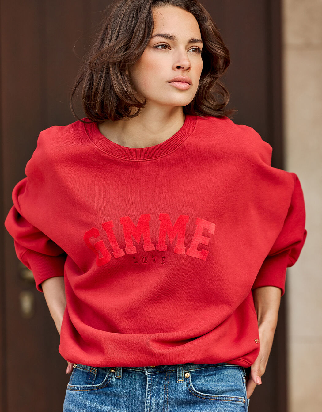 Model standing in the Story Sweater Raspberry Red in organic cotton knit with a GIMME print.