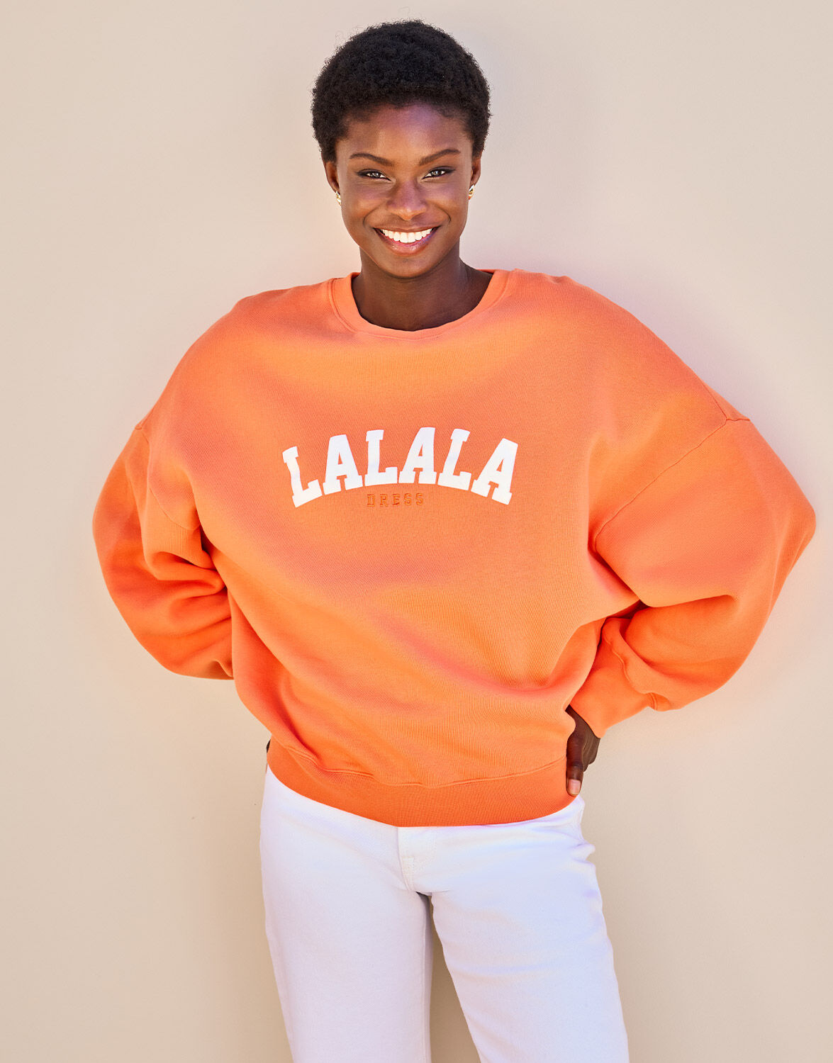 Model standing in the Story Sweater Dutch Orange in organic cotton knit with a LALALA print.