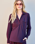 Woman wears an elegant purple blouse with long sleeves and pockets, paired with fashionable sunglasses.