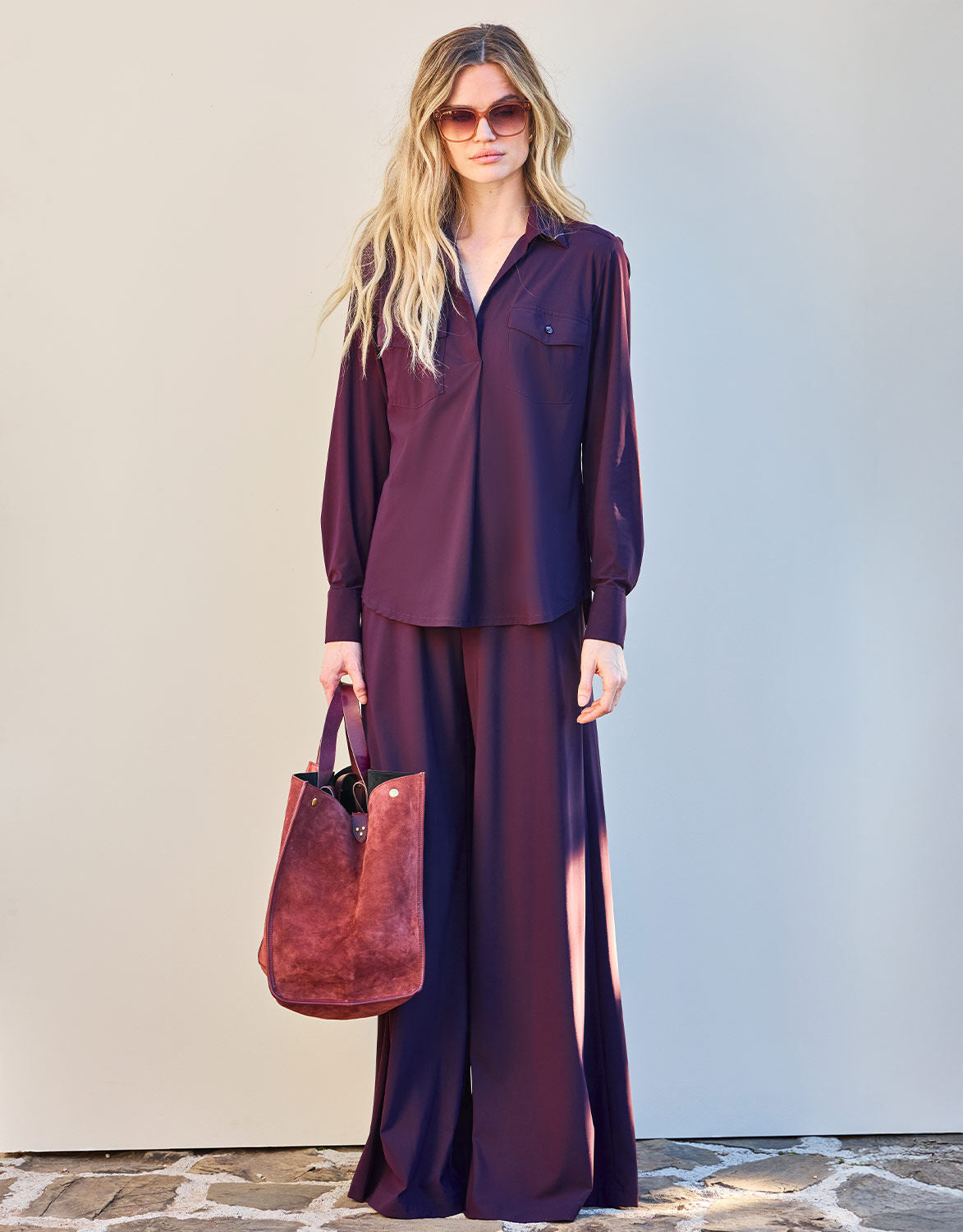 Model standing in the Esmee Deep Aubergine blouse in jersey lycra with a suede tote bag.
