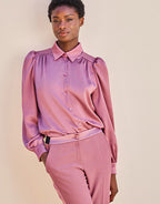 Elegant mauve silk blouse with long sleeves and button closure, paired with matching trousers in a neutral setting.
