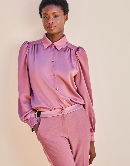 Elegant mauve silk blouse with long sleeves and button closure, paired with matching trousers in a neutral setting.