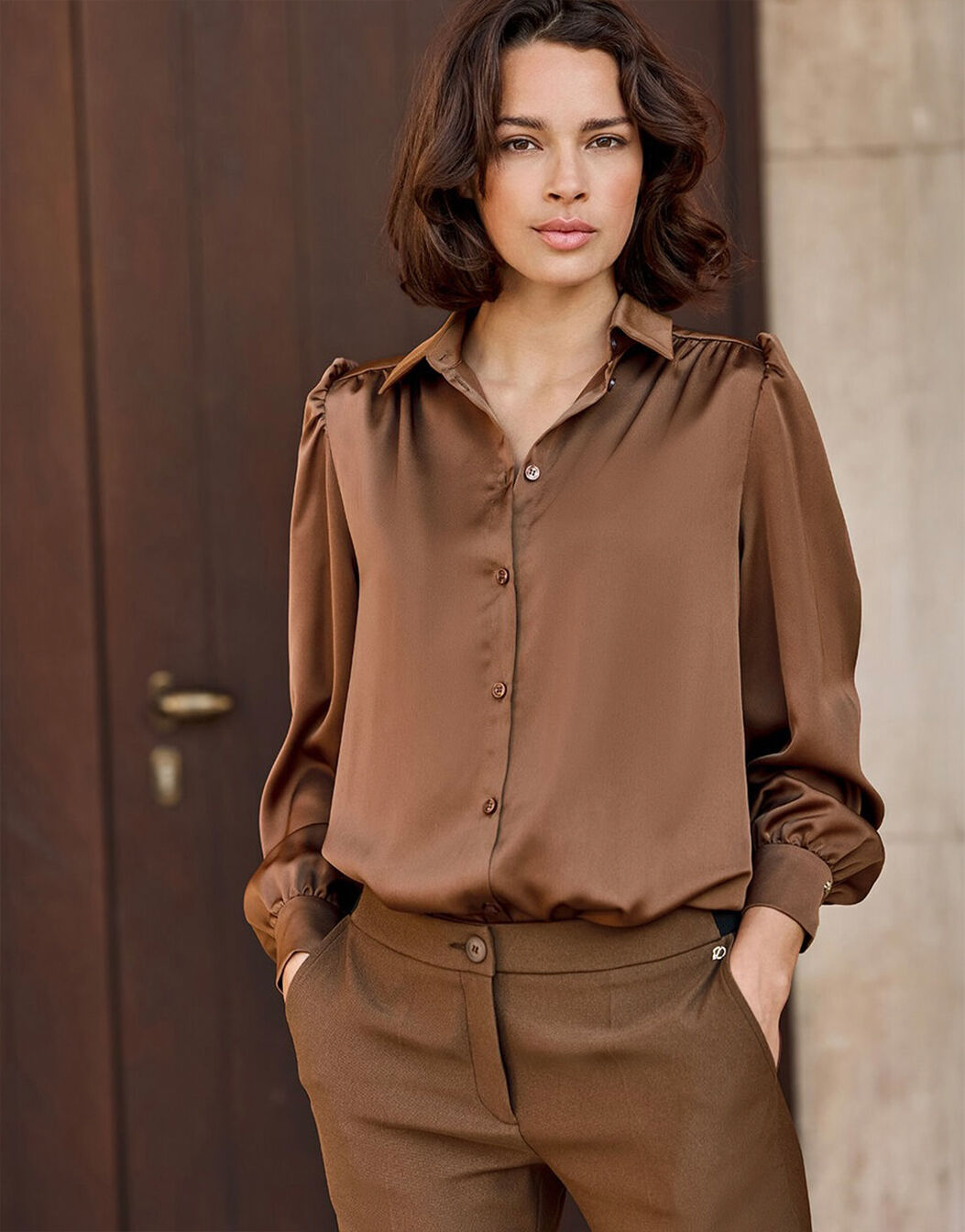 Model standing in the Tilda Cacao Brown blouse in satin with matching trousers.