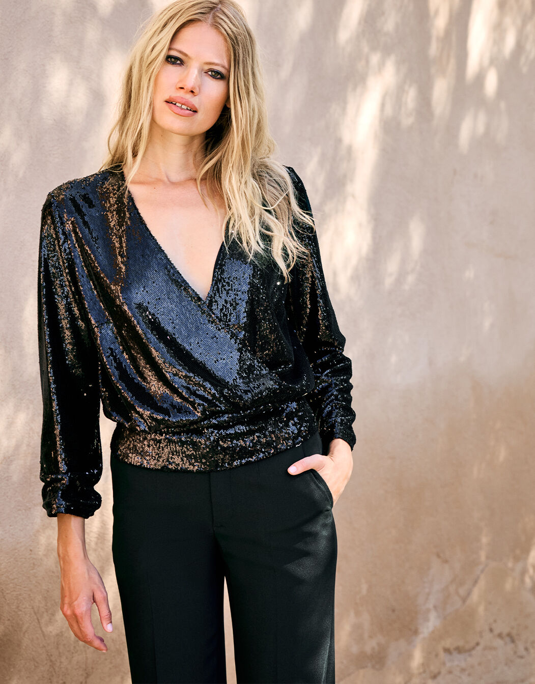 Woman in a chic black sequined long-sleeved shirt and elegant black trousers for a stylish and modern look.