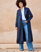 Dark blue satin trench coat worn by a woman with down hair, paired with a white blouse and blue jeans.