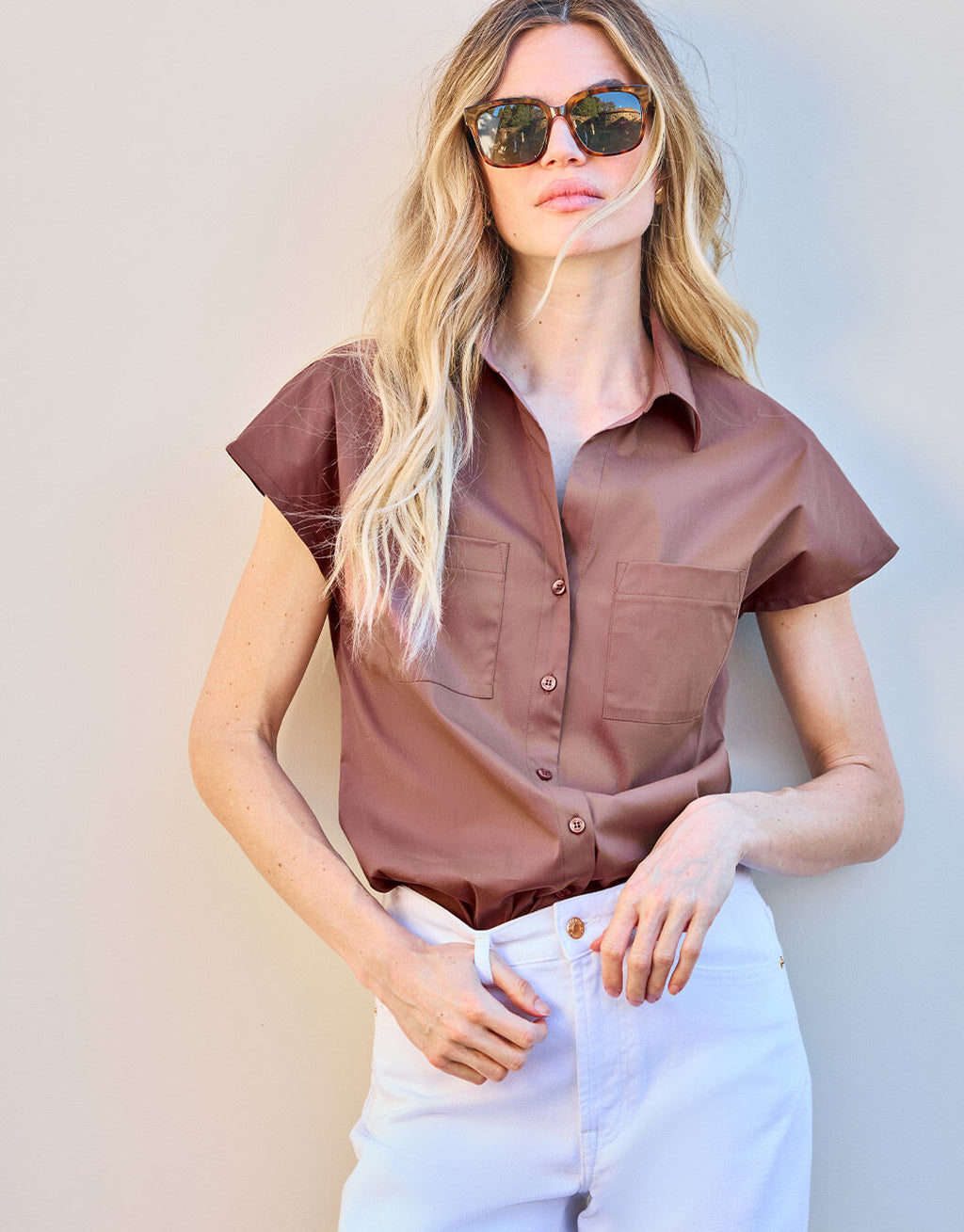 Woman in a brown short-sleeved blouse and white trousers, stylish sunglasses, modern summer fashion.