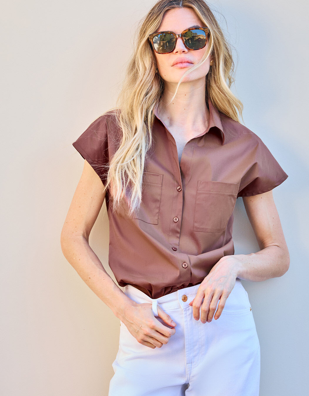 Frau in einer braunen kurzärmligen Bluse und weißer Hose, stilvolle Sonnenbrille, moderne Sommermode.