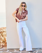 Woman in a stylish brown blouse and wide white trousers poses against a neutral background with natural stones.