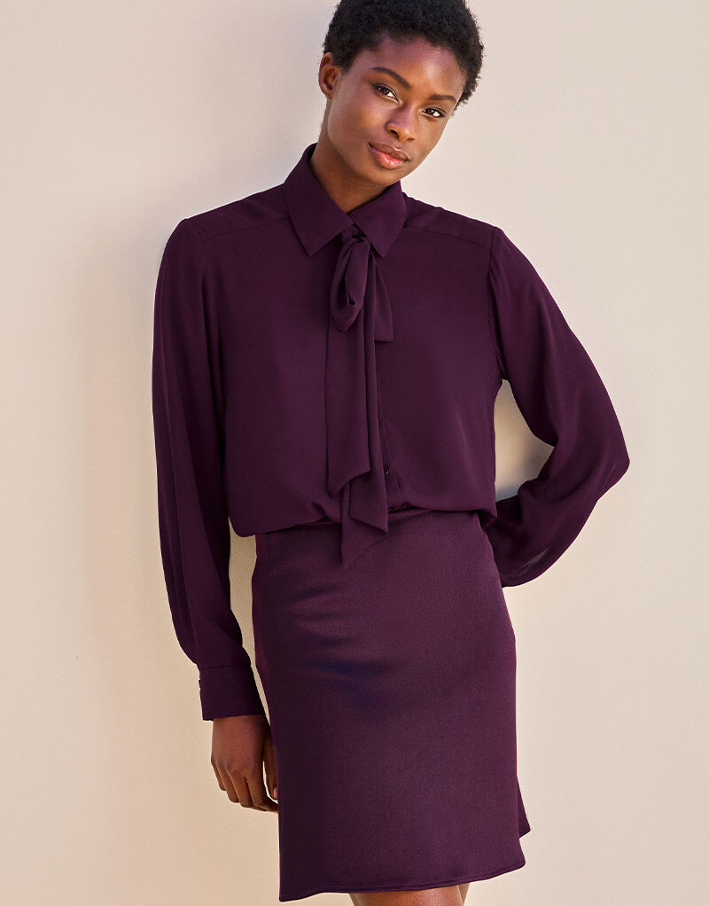 Model standing in the Kris Deep Aubergine blouse in crepe georgette with a pussy bow.