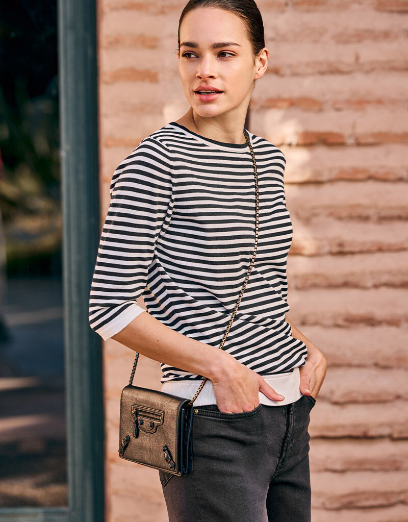 Model standing in the Caitlyn Black Stripe jumper in organic cotton knit with jeans and a small bag.